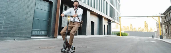 Tutta la lunghezza dell'uomo d'affari in abbigliamento formale cavalcando moderno scooter elettrico vicino alla costruzione, banner — Foto stock