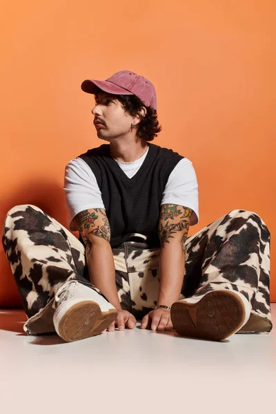 Giovane uomo vestito in abiti alla moda si siede comodamente, trasudando carisma e fiducia nello stile. — Foto stock