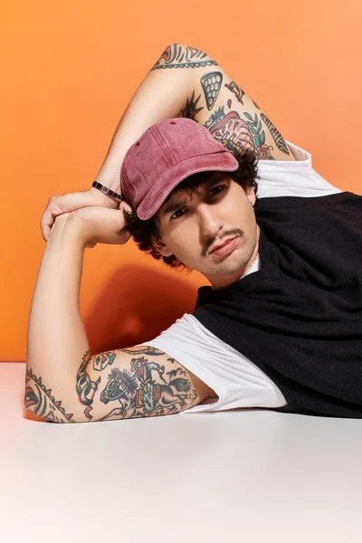 Handsome young man in a trendy outfit lounges casually with a striking orange background. — Stock Photo