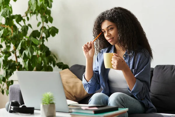 В современной квартире молодая афроамериканка вдумчиво пьет кофе во время работы. — стоковое фото