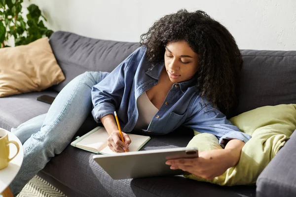 Eine junge Frau macht sich selbstständig, während sie es sich auf ihrem Sofa in einer modernen Wohnung gemütlich macht. — Stockfoto