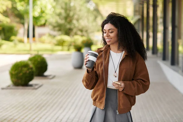 A fashionable young woman walks with a warm drink, embracing autumn's beauty in her stylish outfit. — Stock Photo