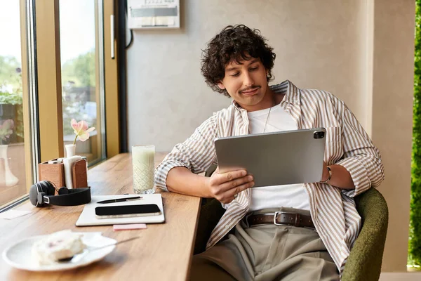 Schöner junger Mann entspannt in einem Café, surft auf einem Tablet und nippt an einem erfrischenden Getränk. — Stockfoto