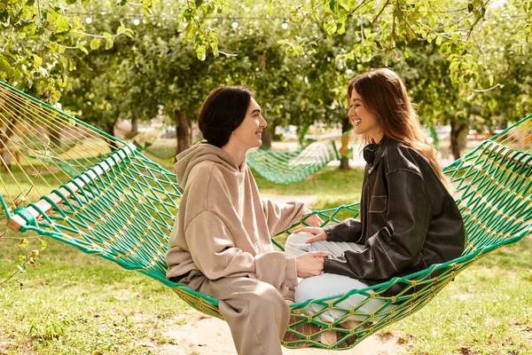 Zwei Liebende lächeln einander an, während sie zusammen in einer Hängematte sitzen, umgeben von üppigem Grün. — Stockfoto