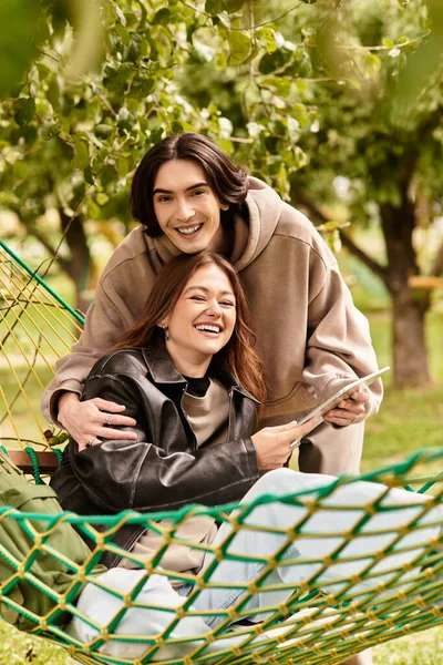 Молодая пара делится радостными моментами в гамаке, окруженный зелеными деревьями и природой красоты. — стоковое фото