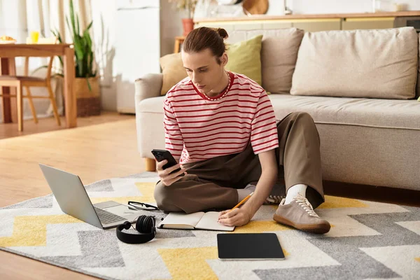 Молодой человек сидит на полу, на телефоне, окруженный блокнотами и ноутбуком. — стоковое фото
