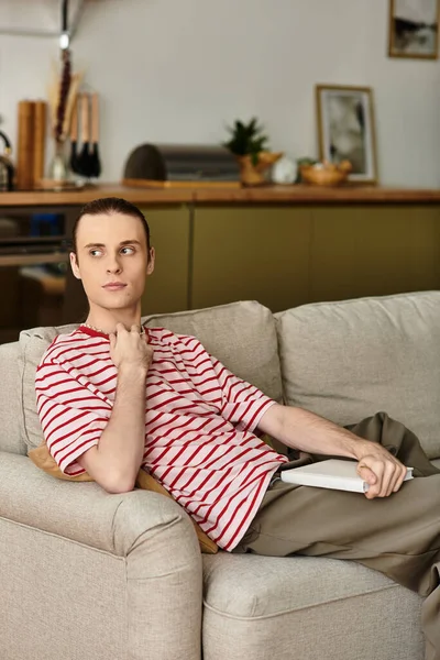 Un jeune homme beau assis sur un canapé confortable, plongé dans la lecture dans un salon élégant. — Photo de stock