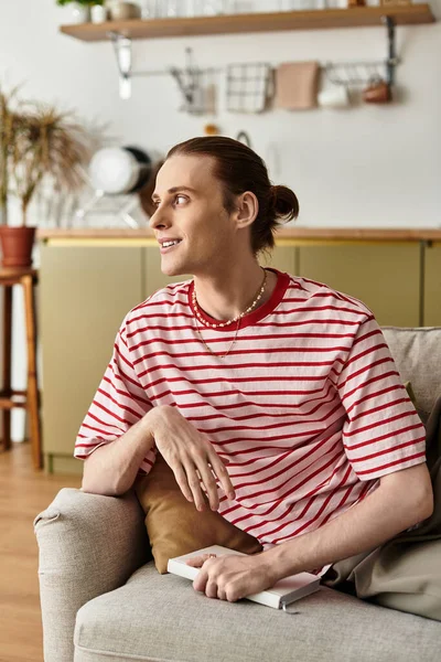 A handsome young man relaxes on a sofa, deep in thought in a bright kitchen. — Stock Photo
