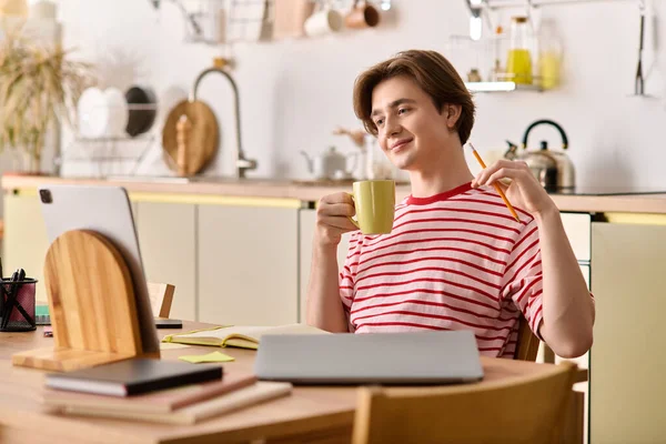 Молодой человек учится дома в своей стильной квартире, потягивая чай, сосредоточившись на ноутбуке. — стоковое фото