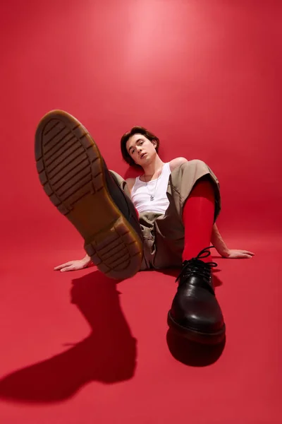 Giovane uomo posa con fiducia in pantaloni alla moda e una canotta con uno sfondo rosso. — Foto stock