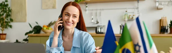 A woman with red hair happily teaches a language lesson online, using her smartphone, banner — стоковое фото