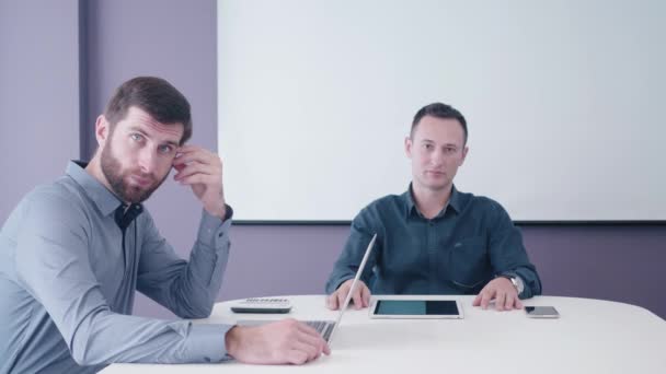 Two middle-aged businessmen sitting with tablet and laptop in the meeting room and sceptical listening their interlocutor behind the camera finally rejecting him — Stock Video