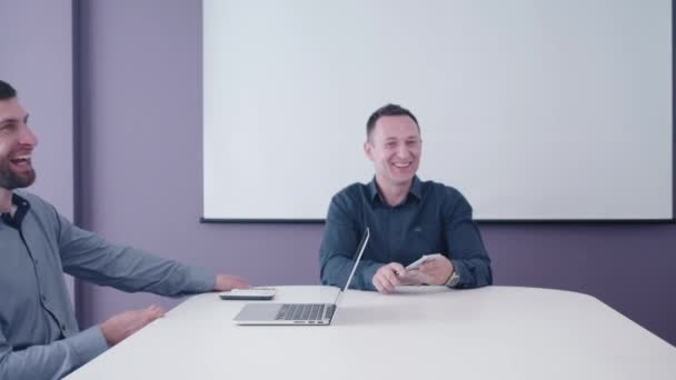 Young startup developer comes with fun idea to his two business partners who sitting in the meeting room and laughing and discuss it with them demonstrating on tablet screen — Stock Video