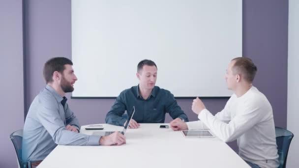 Young startup developer comes to two middle-aged corporate managers sitting in the meeting room for consideration his ideas on tablet screen 4K shooting — Stock Video