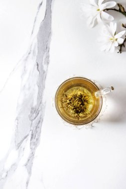 Cam fincan yeşil çay ile bahar beyaz mermer doku arka plan üzerinde beyaz Manolya çiçek açan dalları çiçekler. Üstten Görünüm, kopya alanı.