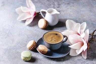 Mavi kupa siyah espresso ile Fransız tatlı macaroons kahve krema ve bahar çiçek Manolya dalları gri doku arka plan üzerinde. Üstten Görünüm, uzay.