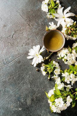 Geleneksel seramik fincan yeşil çay bahar çiçekleri ile beyaz Manolya ve kiraz çiçek açan dalları koyu mavi doku arka plan üzerinde. Üstten Görünüm, kopya alanı.