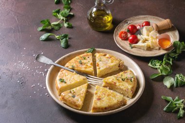 Seramik tabak içinde malzemelerle koyu kahverengi doku arka plan üzerinde hizmet pastırma ile İspanyol patates omlet tortilla dilimlenmiş.