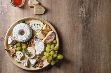 Fransızca peynir peynir tabağı yelpazesine tatlım, ceviz, ekmek ve üzüm seramik plaka üzerinde ahşap doku arka plan üzerinde servis. Üstten Görünüm, kopya alanı.