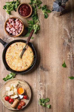 İspanyol patates omlet tortilla pastırma ile sos ve malzemeler yukarıda ile dökme demir tavada ahşap arka plan üzerinde servis. Üstten Görünüm, uzay.