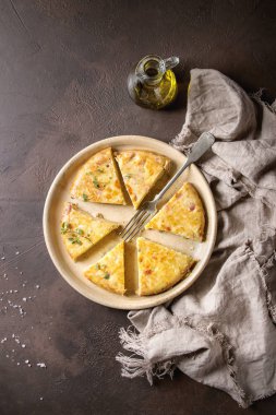 Seramik tabak içinde zeytin yağı ve keten kumaş ile koyu kahverengi doku arka plan üzerinde servis pastırma ile İspanyol patates omlet tortilla dilimlenmiş. Üstten Görünüm, uzay.