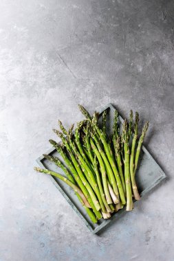 Çiğ çiğ organik yeşil kuşkonmaz içinde gri doku arka plan üzerinde ahşap tepsi. Üstten Görünüm, kopya alanı.