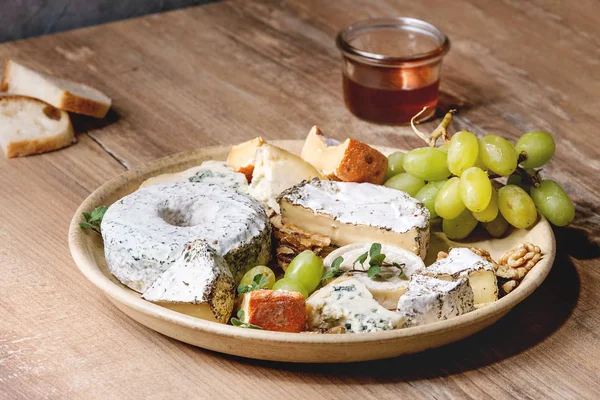 チーズ プレート フランス産チーズ各種木製テーブルに蜂蜜 クルミ セラミック プレートのブドウを添えてください クローズ アップ — ストック写真