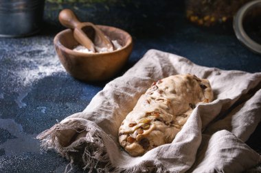 Christmas cake, geleneksel Alman şenlikli pişirme. Kepekli hamur stollen hazırlık ile keten peçete üzerinde koyu mavi doku arka plan üzerinde un, Kuru üzüm, köknar ağacı kase. Rustik tarzı