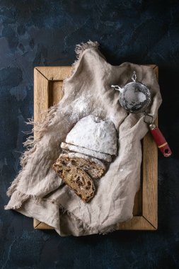 Noel kek dilimlenmiş, geleneksel Alman şenlikli pişirme. Kepekli stollen kuru üzüm ve keten peçete, ahşap tepsi, koyu mavi arka plan üzerinde vintage elek pudra şekeri ile. Üstten görünüm, uzay