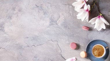 Mavi ile siyah espresso kahve fincan tatlı macaroons Fransız ve çiçekler Manolya dalları gri doku arka plan üzerinde bahar. Üstten Görünüm alanı. Bahar tebrik kartı, duvar kağıtları