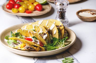 Çeşitli vejetaryen Mısır Tacos sebze, yeşil salata, biber biber domates ile seramik tabak ve beyaz mermer mutfak masasında malzemelerle krem soslar servis. Yakın çekim