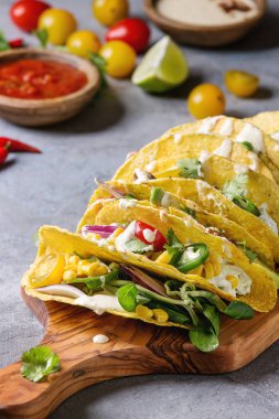 Çeşitli vejetaryen Mısır Tacos sebze, yeşil salata, biber biber domates ile ahşap kesme tahtası ve krem soslar malzemelerle gri doku arka plan üzerinde servis. Yakın çekim
