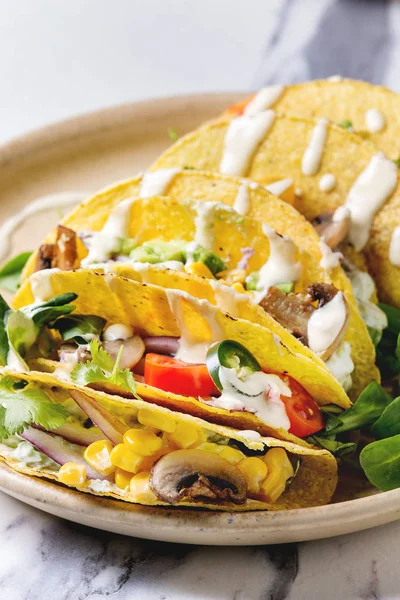 Çeşitli vejetaryen Mısır Tacos sebze, yeşil salata, biber biber domates ile seramik tabak ve beyaz mermer mutfak masasında malzemelerle krem soslar servis. Yakın çekim