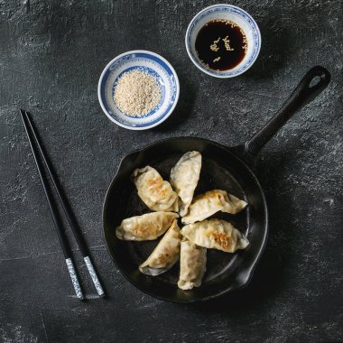 Asya köfte Gyozas potstickers siyah doku arka plan üzerinde chopsticks ve kase soya susam sos ile servis dökme demir tava, kızarmış. Üstten Görünüm, uzay.