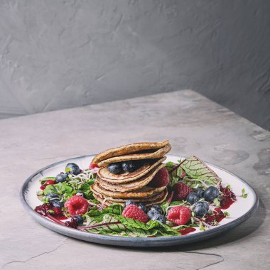 Vegan nohut krep gri mutfak masasının üzerinde plaka yeşil salata yaprakları genç pancar, Brüksel lahanası, çilek, berry sos ile servis. Uzay kopyalayın. Sağlıklı beslenme. Tonlu görüntü