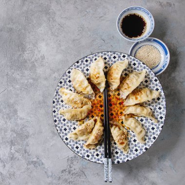 Asya köfte Gyozas potstickers beyaz mavi seramik plaka üzerinde gri doku arka plan üzerinde chopsticks ve kase soya susam sos ile servis. Üstten Görünüm, kopya alanı.