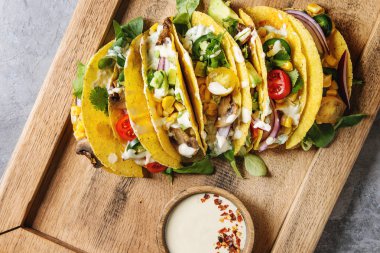 Çeşitli vejetaryen Mısır Tacos sebze, yeşil salata, biber ile krema sosu ile ahşap tepsi üzerinde gri doku arka plan üzerinde servis. Üstten görünüm, uzay.