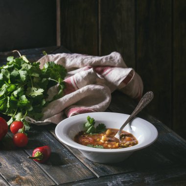 Vejetaryen sıcak havuç domates bezelye patates çorbası, plaka ve vintage alüminyum tavada eski ahşap tahta masa üzerinde taze kişniş ve domates ile servis. Karanlık rustik tarzı. Kare görüntü