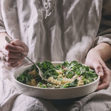 Kadın oturuyor tutun ve vegan quinoa salata lahana ile yemek, genç pancar yaprakları, granat tohumu, avokado beyaz tabağına dilimlenmiş. Sağlıklı beslenme. Tonlu görüntü