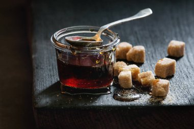 Cam karamel ev yapımı sıvı şeffaf kahverengi şeker kavanoz duran siyah ahşap tahta kaşıkla ve küp şeker. Yakın çekim. Gün ışığı