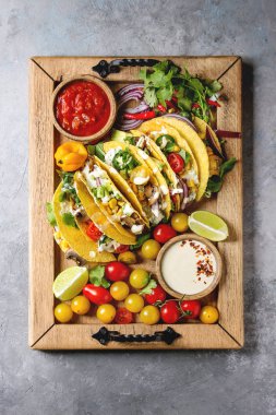 Çeşitli vejetaryen Mısır Tacos sebze, yeşil salata, biber biber domates ile ahşap tepsi ve krem soslar malzemelerle gri doku arka plan üzerinde servis. Üstten görünüm, uzay.
