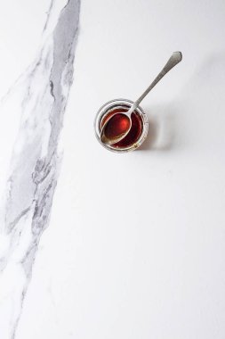 Ev yapımı sıvı şeffaf kahverengi şeker karamel beyaz mermer zemin üzerinde vintage kaşık ile cam kavanoza. Düz lay, uzay.