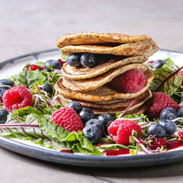 Vegan chickpea pancakes served in plate with green salad young beetroot leaves, sprouts, berries, berry sauce over grey kitchen table. Close up. Healthy eating