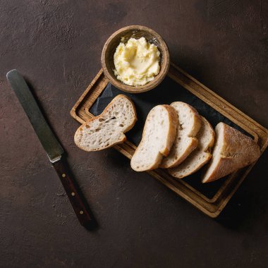 Taze somun dilimlenmiş esnaf ahşap arduvaz koyu kahverengi doku arka plan üzerinde kurulu hizmet üzerinde tereyağı ve vintage bıçakla baget ekmek pişirdim. Üstten Görünüm, kopya alanı.