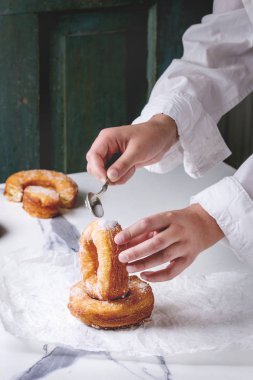 Oğlanın elini tutun ev yapımı puf böreği derin kızarmış çörek veya cronuts Instalar şekerli Kağıt beyaz mermer mutfak masasının üzerinde buruşuk..