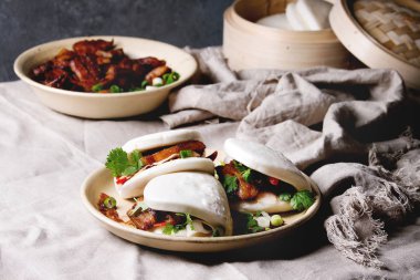 Asya sandviç Gua bao buns domuz eti, yeşil ve sebzeler ile keten masa örtüsü seramik tabak masaya servis ile atmak. Asya tarzı hızlı yiyecek yemek.