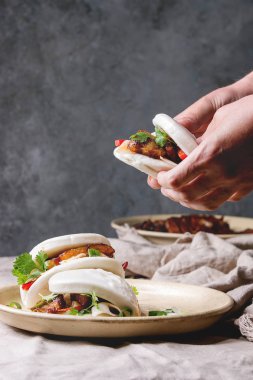 Adamın elleri Asya sandviç buğulama gua bao buns domuz eti, yeşil ve sebzeler ile keten masa örtüsü seramik tabak masaya servis ile tutun. Asya tarzı hızlı yiyecek yemek.