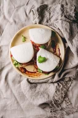 Asya sandviç Gua bao buns domuz eti, yeşil ve seramik tabak içinde keten masa örtüsü üzerinde hizmet sebze ile atmak. Asya tarzı hızlı yiyecek yemek. Düz lay, uzay