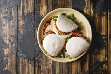 Asya sandviç Gua bao buns domuz eti, yeşil ve koyu ahşap tahta arka plan üzerinde seramik tabak içinde servis sebze ile atmak. Asya tarzı hızlı yiyecek yemek. Düz lay, uzay