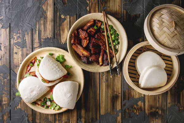 Asya sandviç Gua bao buns domuz eti, yeşil ve koyu ahşap tahta arka plan üzerinde seramik tabak içinde servis sebze ile atmak. Asya tarzı hızlı yiyecek yemek. Düz lay, uzay